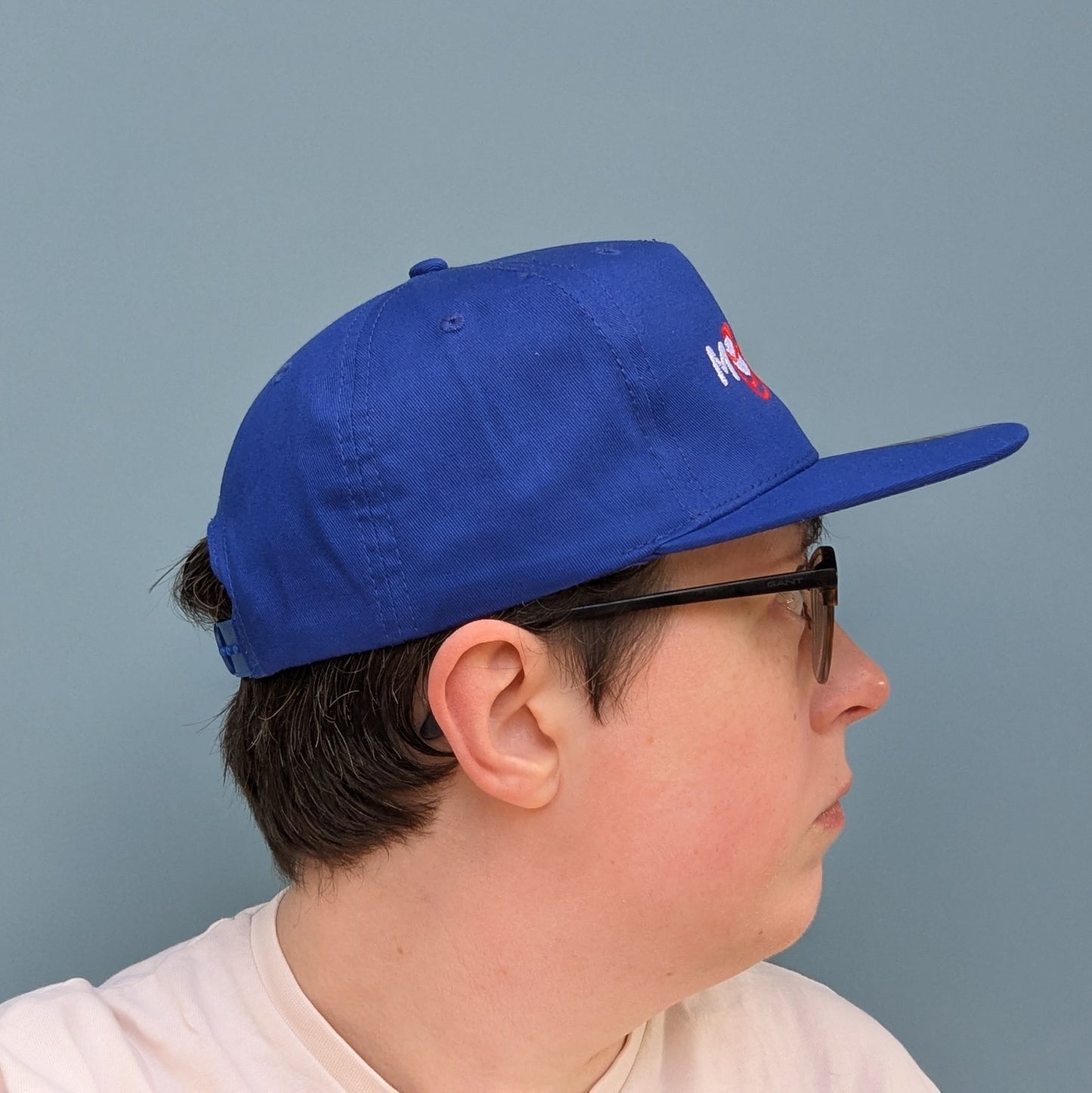 Side facing view on a person wearing a blue cap with 'Moon Joy' text, featuring a red route and Rise, against a light background