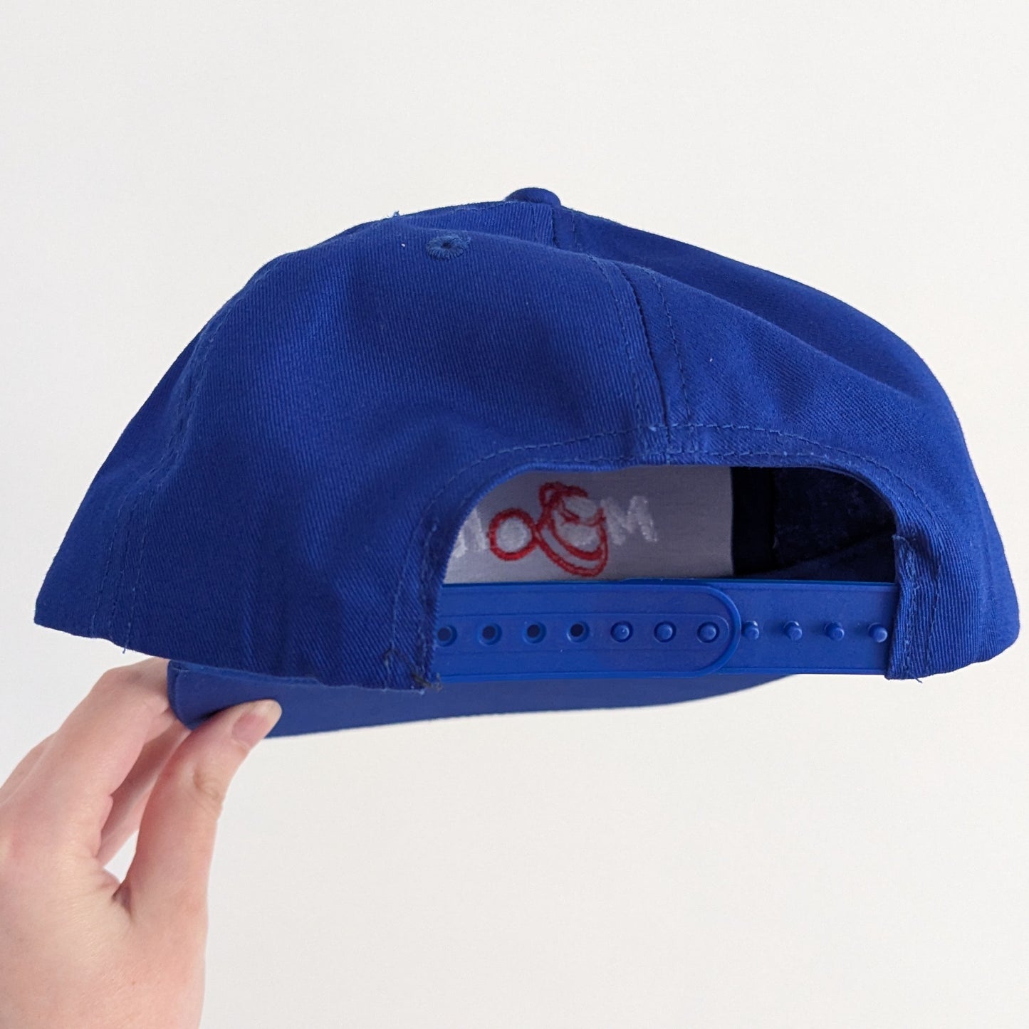 Back of a blue cap, showing it's snap adjuster, against a white background