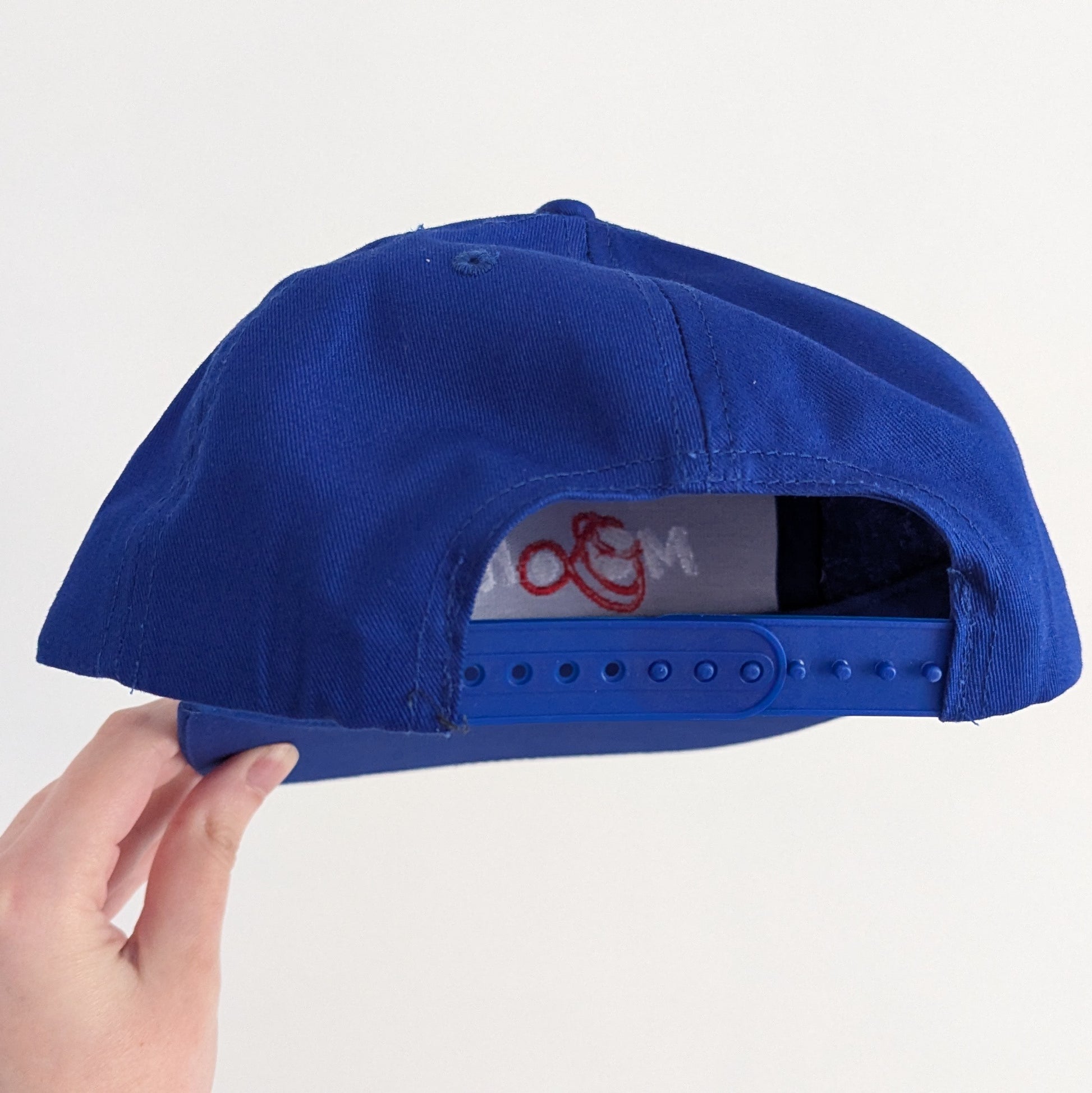 Back of a blue cap, showing it's snap adjuster, against a white background