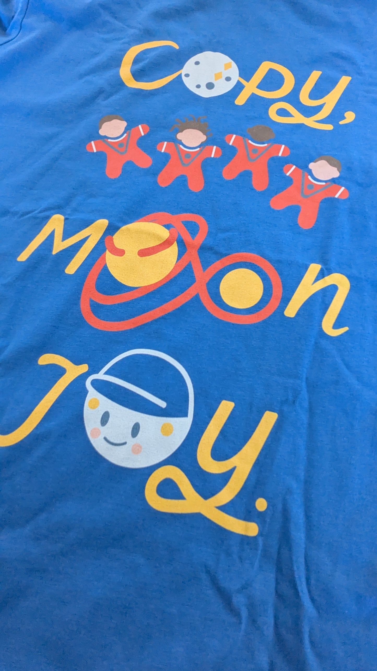 Close up of a mindful blue t-shirt with colourful graphics and text saying 'copy, moon joy'. This showcases the texture of the print on the t-shirt.