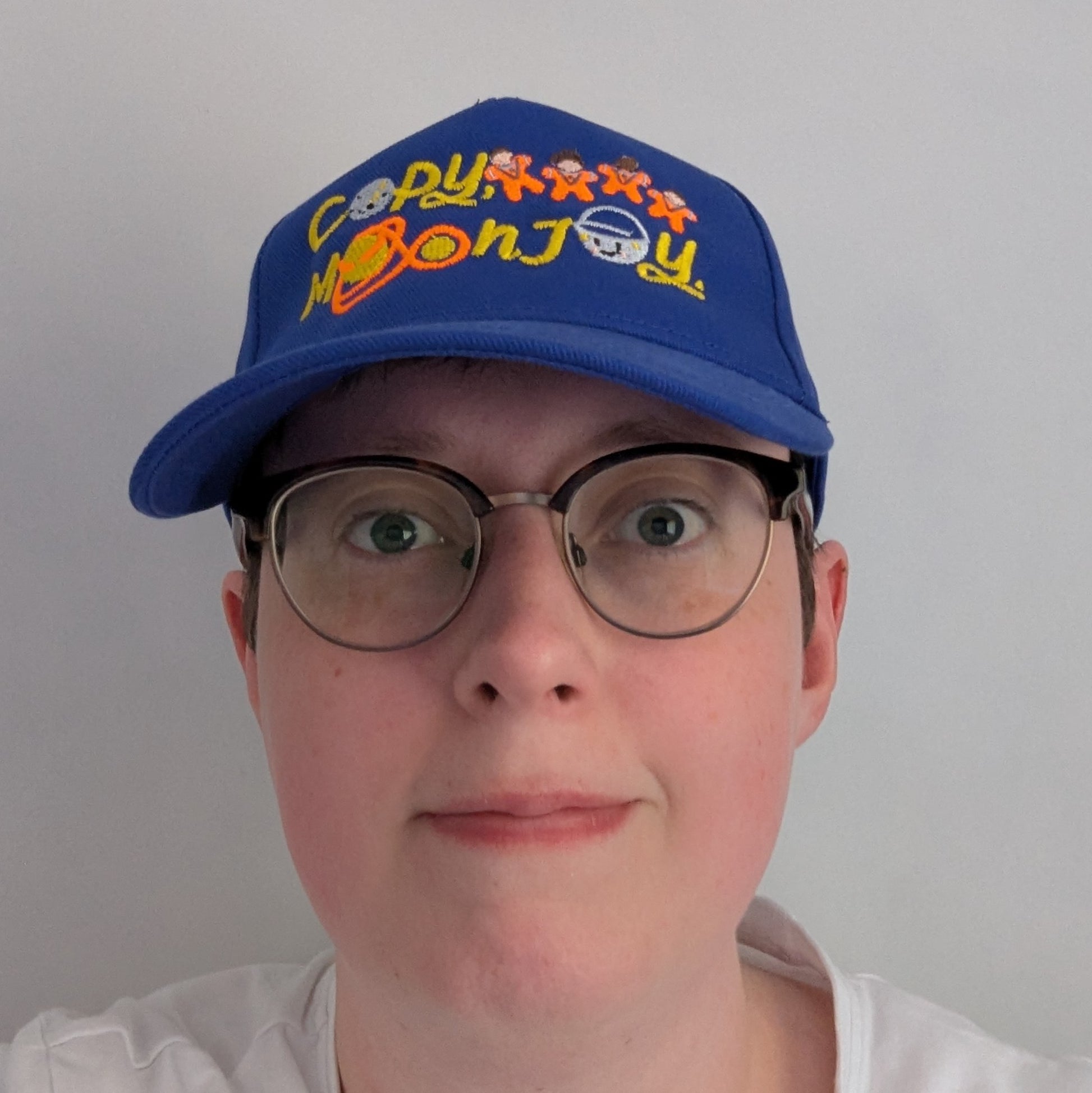 Bright blue adults blue cap with colourful text that reads Copy, Moon Joy. Accompanying text includes graphics.The product is on top of a persons head looking forward, on a white background.
