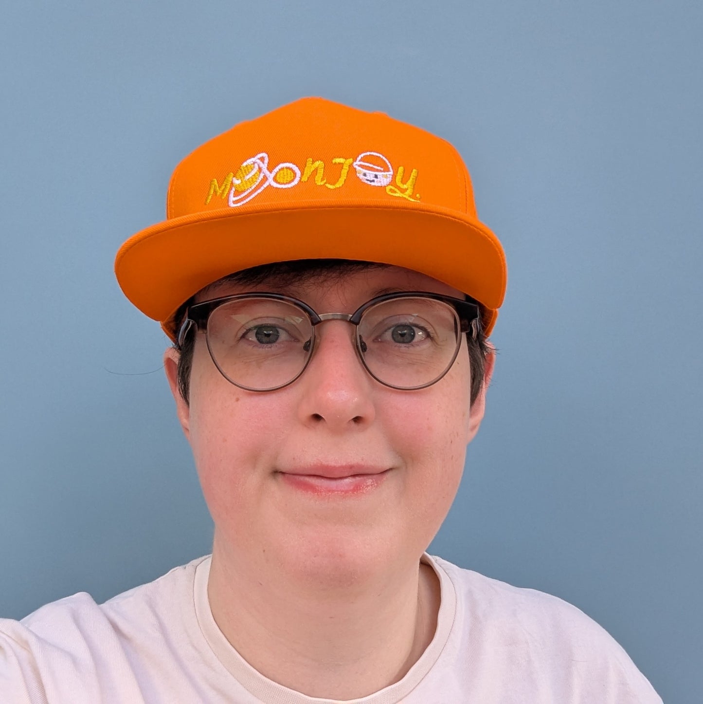 Front facing person wearing orange snapback cap with 'Moon Joy' text, featuring a white route and Rise, against a light background