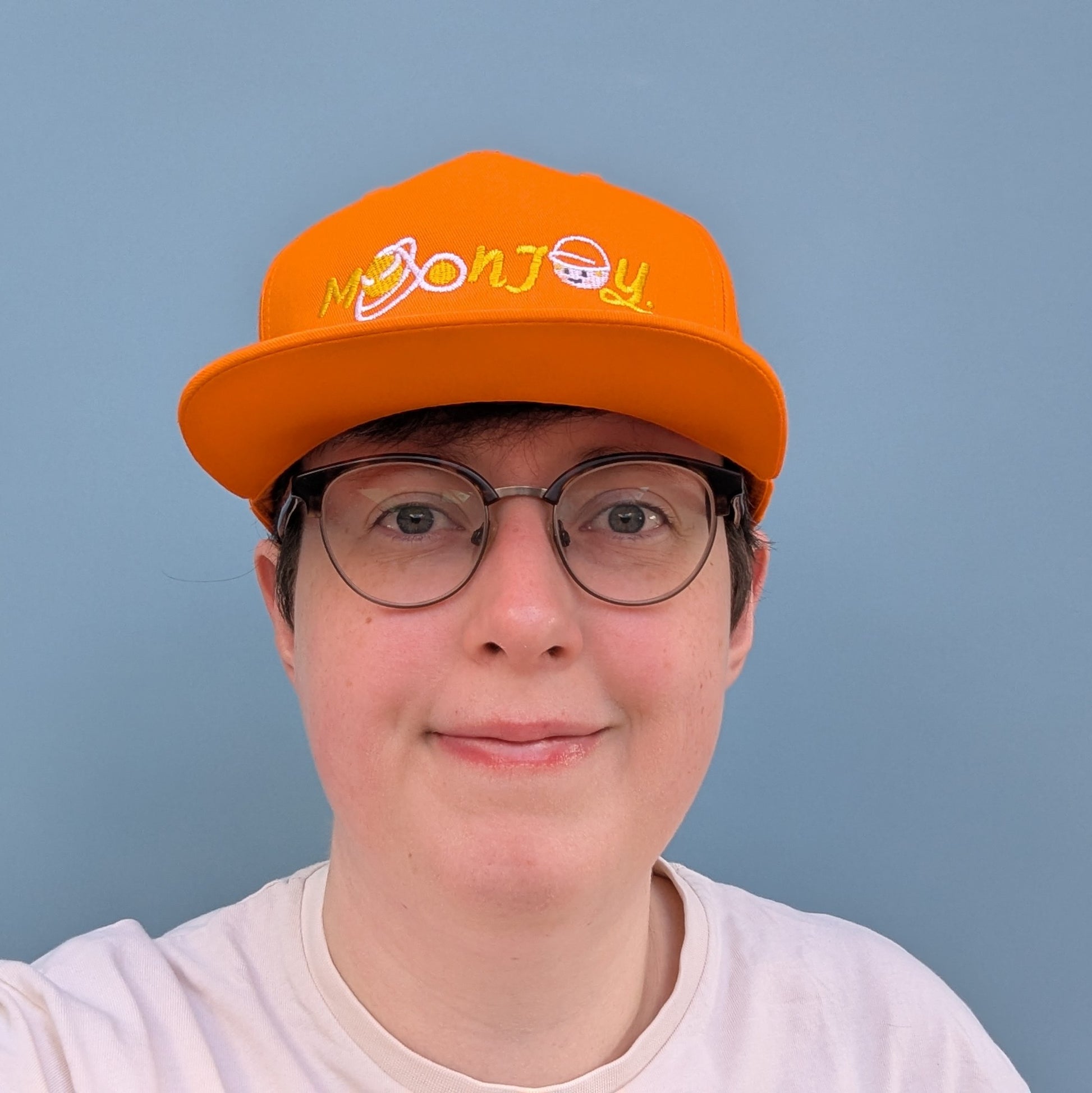 Front facing person wearing orange snapback cap with 'Moon Joy' text, featuring a white route and Rise, against a light background