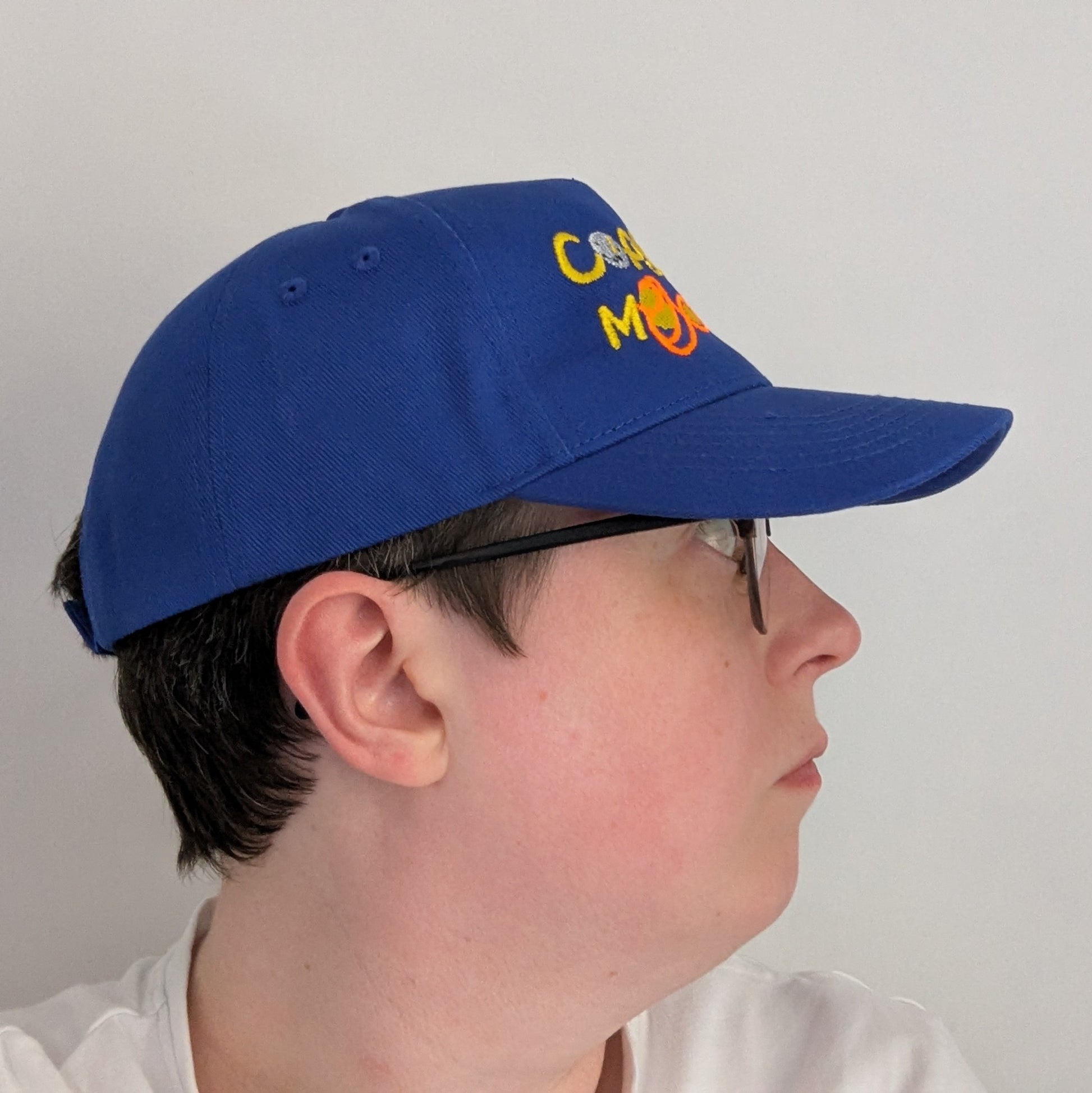 Bright blue adults blue cap with colourful text that reads Copy, Moon Joy. Accompanying text includes graphics.The product is on top of a persons head looking to the right, on a white background.
